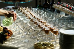 Server pours champagne into dozens of glasses arranged on a banquet table, with fruit and desserts nearby.