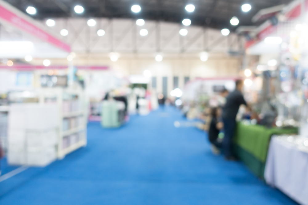 Blurry view of a convention or trade show floor with vendor booths along a blue carpet.