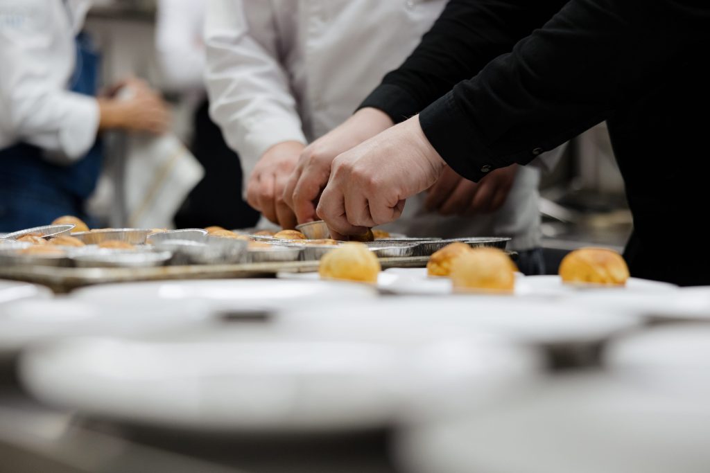 Hands of bakers shaping pastry treats on metal trays in a busy kitchen