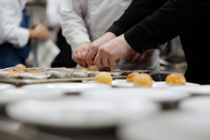 Hands of bakers shaping pastry treats on metal trays in a busy kitchen